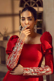 Woman in a red dress with embellished sleeves posing indoors.
