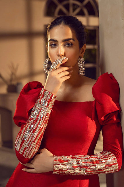 Woman in a red dress with embellished sleeves posing indoors.