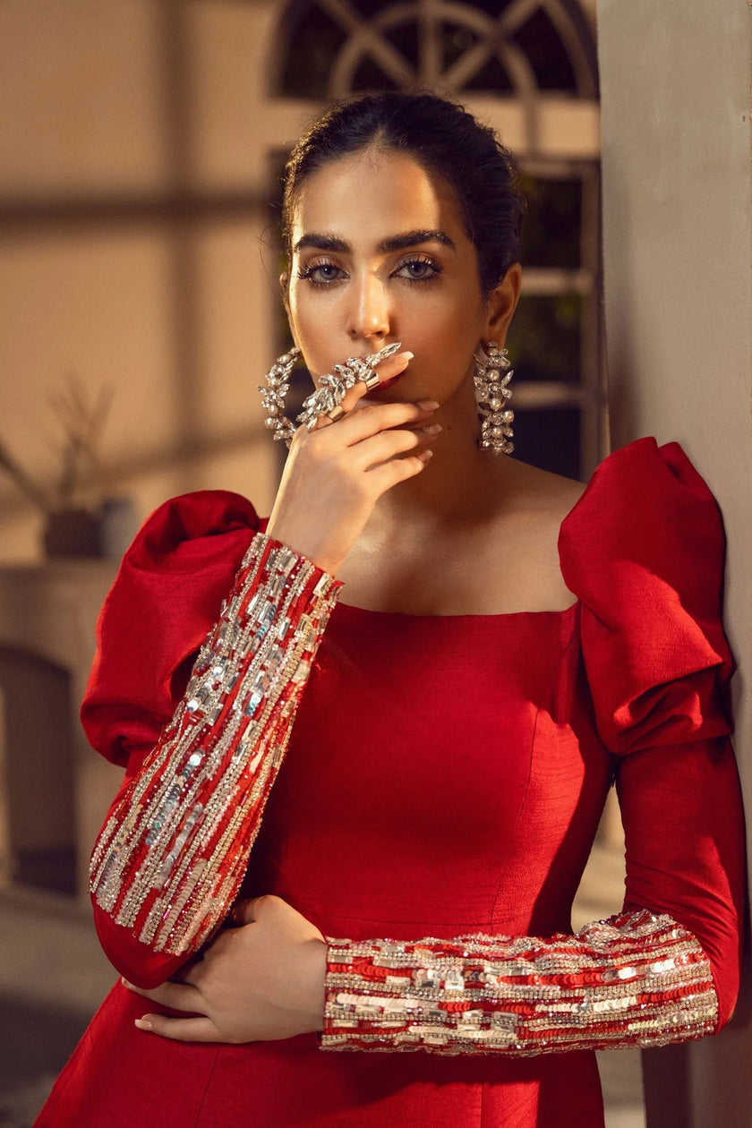 Woman in a red dress with embellished sleeves posing indoors.