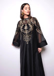Woman wearing a black dress with gold embroidery on a white background