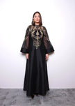 Woman wearing a black dress with gold embroidery against a white background