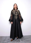 Woman wearing a black dress with gold embroidery against a white background