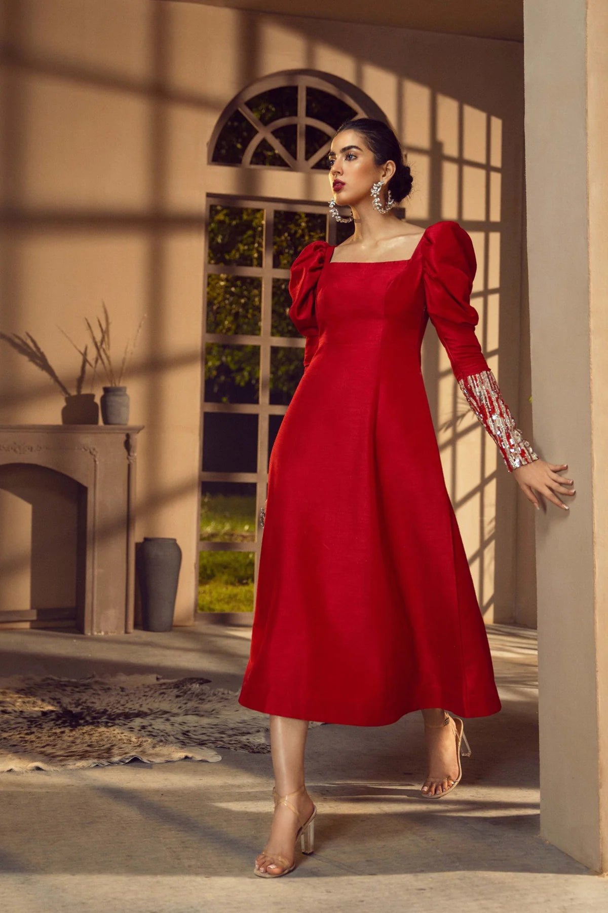 Woman in a red dress standing in a sunlit room with decorative elements.