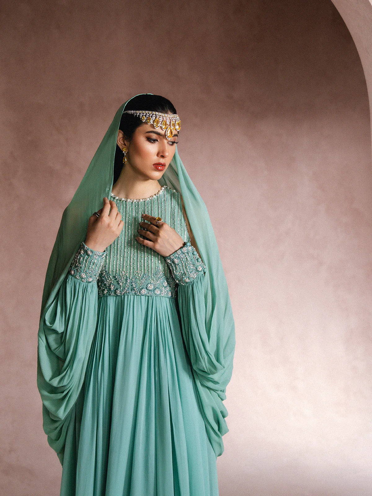 Woman wearing a teal dress with intricate detailing against a beige background