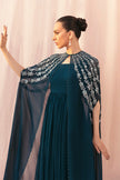 Woman wearing a dark blue dress with an embroidered cape against a light pink background
