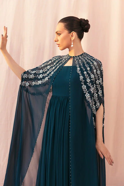 Woman wearing a dark blue dress with an embroidered cape against a light pink background