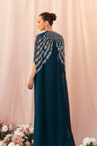 Woman wearing a teal dress with floral embellishments against a pink curtain background.